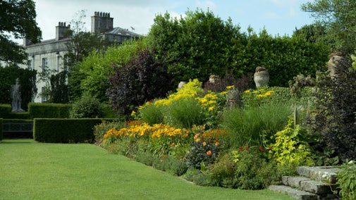 The garden at Plas Newydd Country House and Gardens, Anglesey, Wales, in full bloom in summer with house in the background.